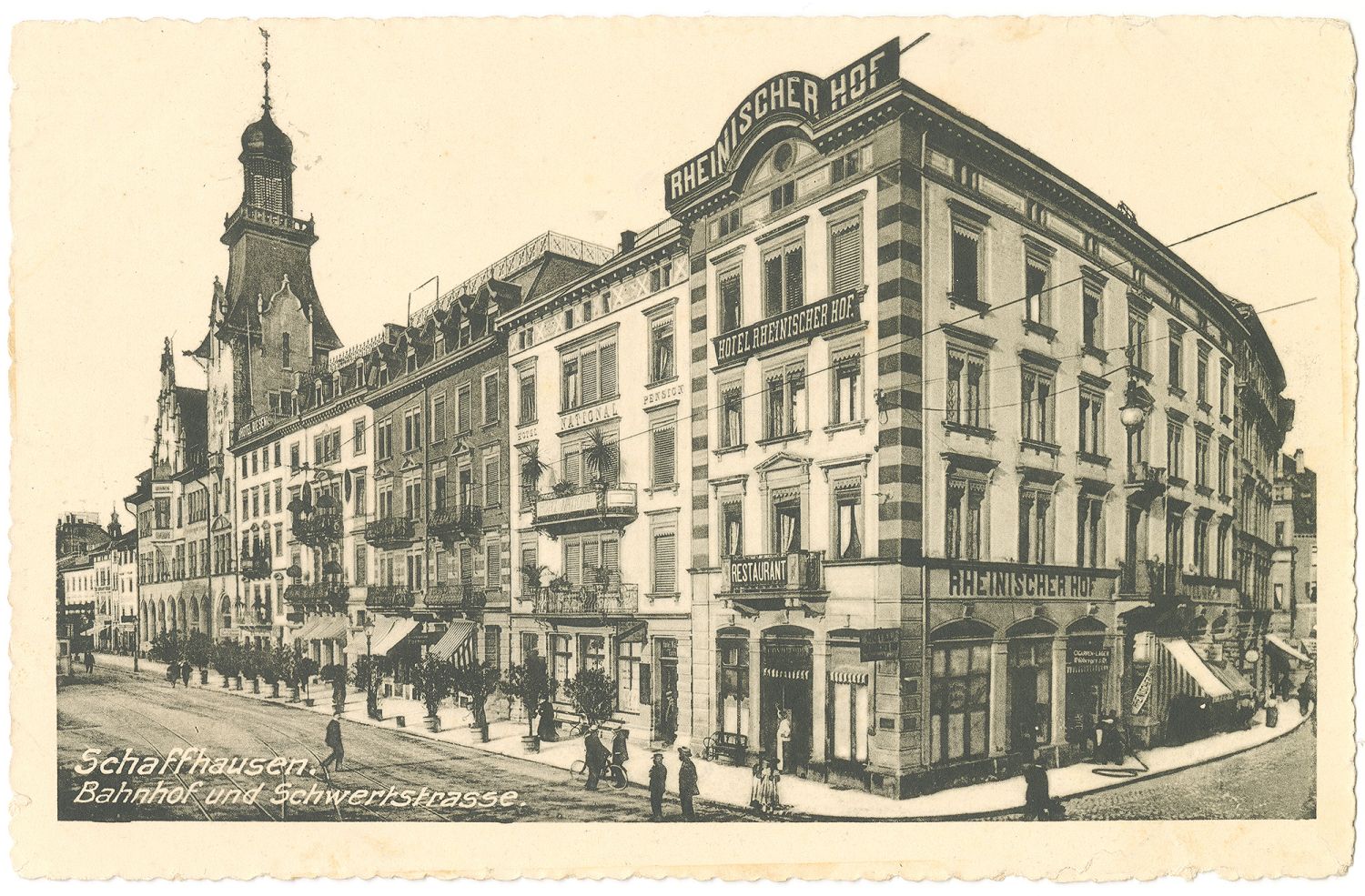 Das Bild zeigt eine detailreich gezeichnete Postkarte der Bahnhofstrasse um ca. <time datetime="1910">1910</time>. Die Postkarte ist in Schwarz-Weiss gedruckt und hat einen Sepia-Effekt, sie sieht etwas vergilbt aus. In der Ecke Bahnhofstrasse-Schwertstrasse steht das stolze Hotel «Rheinischer Hof», welcher <time datetime="1870">1870</time>/<time datetime="1871">71</time> erbaut wurde. Auf der Bahnhofstrasse sieht man Tramgeleise und Karrenspuren der Pferdefuhrwerke. Die Bahnhofstrasse wird von Bäumchen in Pflanztöpfen gesäumt, es gibt Geschäfte mit Sonnenstoren und es sind Menschen zu Fuss unterwegs. Die Hausfassaden sowohl an der Bahnhofstrasse als auch an der Schwertstrasse sind sehr detailreich gestaltet, im Stil des Spätklassizismus.